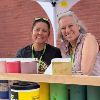 Two ladies smiling with paint canisters in front of them
