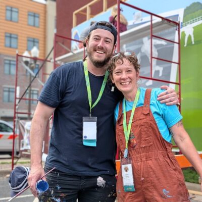 Two artists in paint covered clothes smile at the camera
