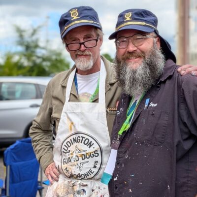 Two artists in paint splattered clothes and matching hats smiling together