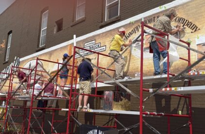Multiple artists scattered across scaffolding painting a long mural