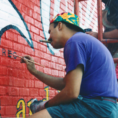 historical photo of man in purple shirt and a cigar painting letters on a red mural