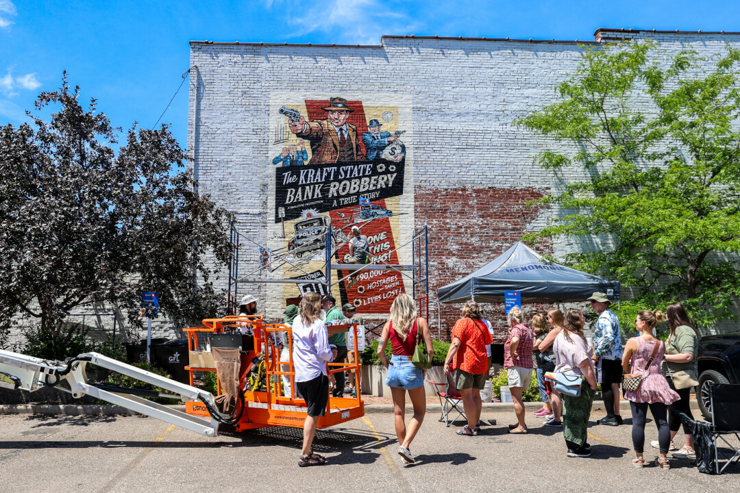Group of people in the street admiring artists painting a large mural on the brick wall
