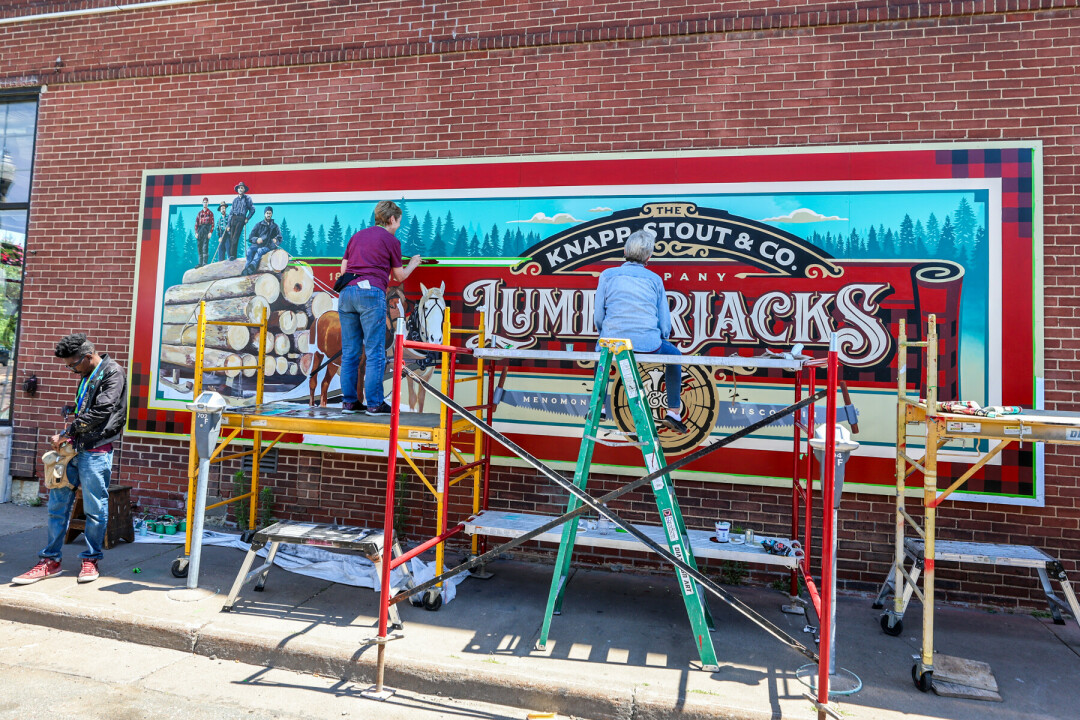 Artists standing on scaffolding painting large mural on a brick wall