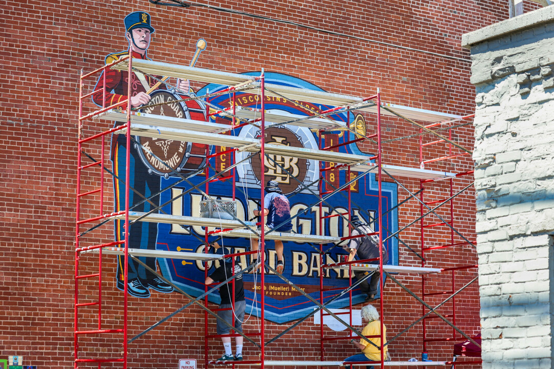 Large brick wall with scaffolding in front of it holding people painting mural