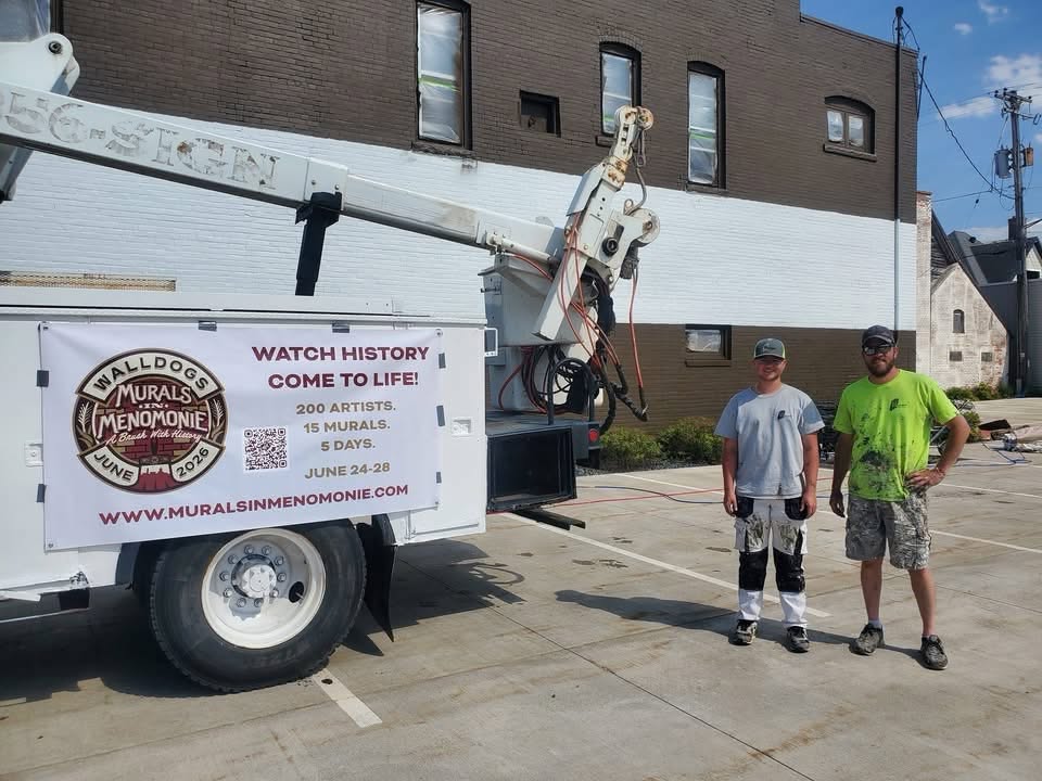 Two guys in dirty paint covered clothes stand by a large truck with a lift bucket