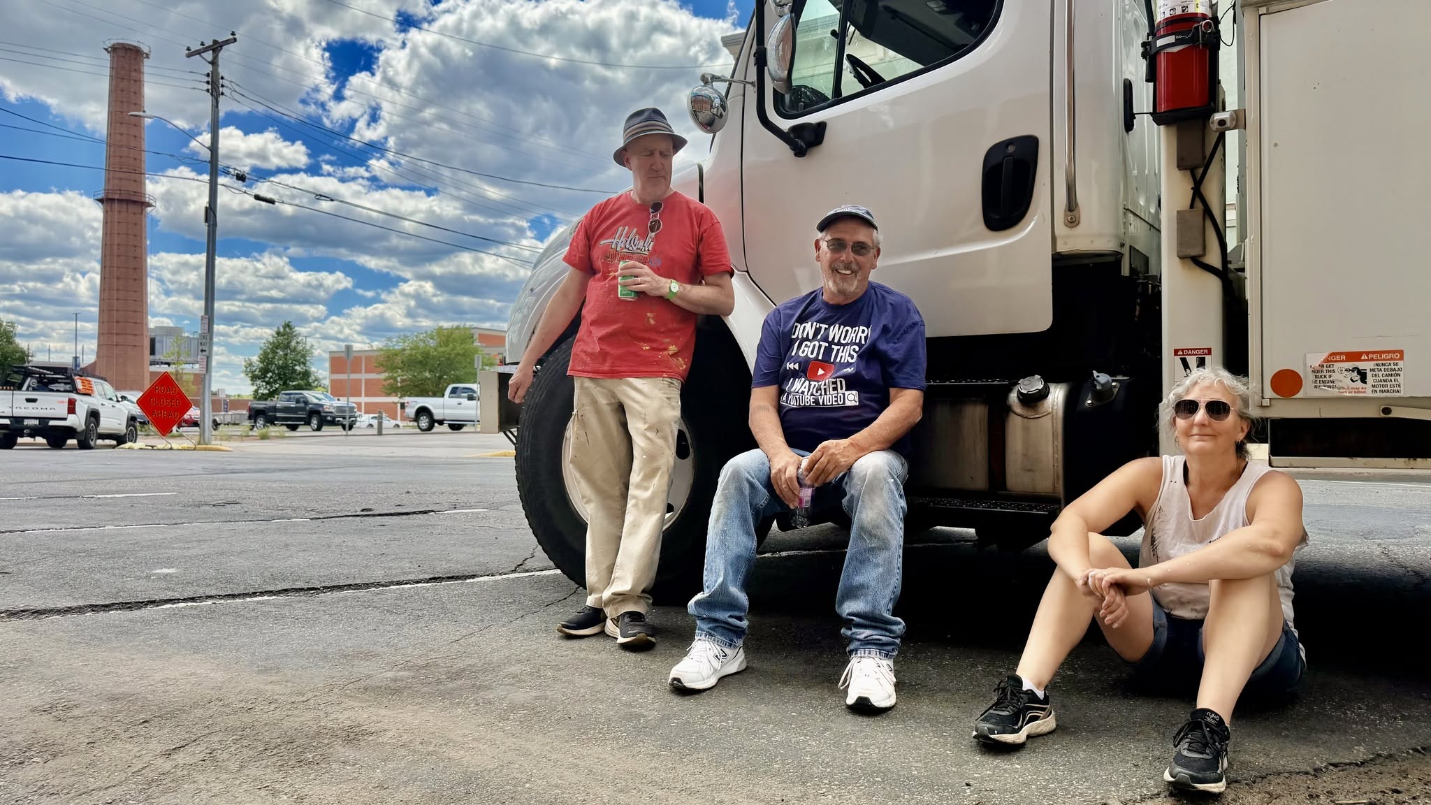 Artists and volunteers resting beside a large delivery truck on a partly cloudy day