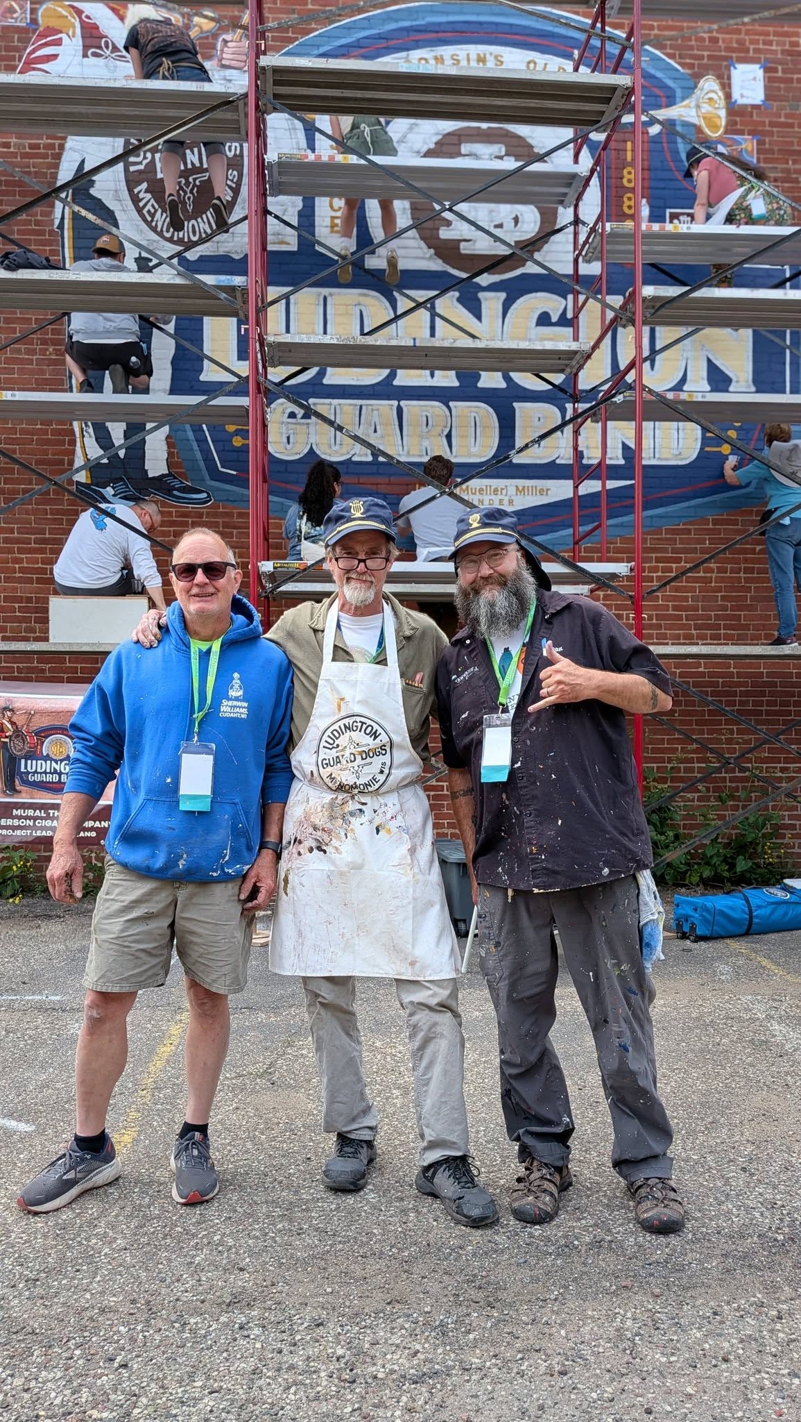 Three artists in paint covered clothes posing in front of a mural being painted