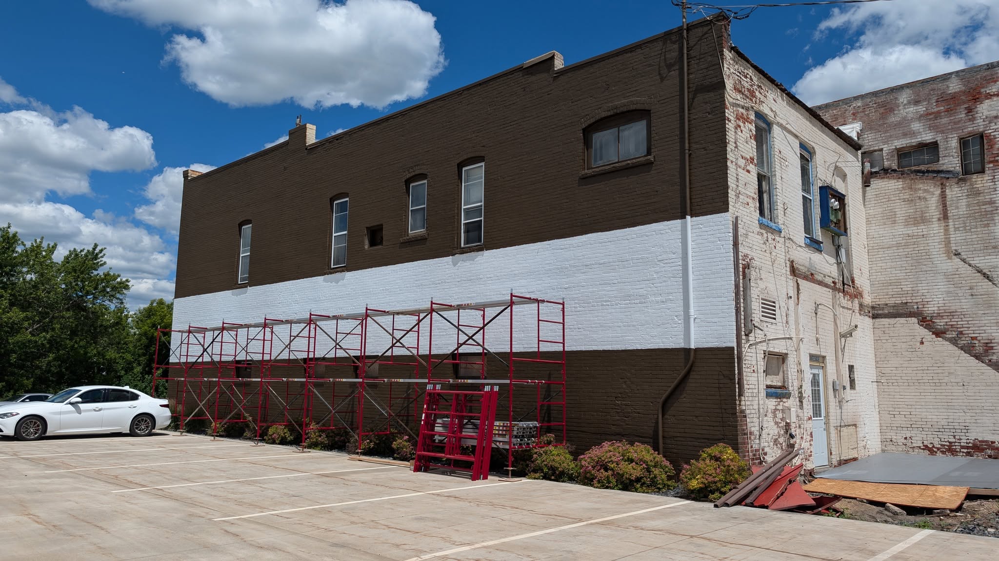 Large long brick wall painted with white strip and scaffolding in front of it, ready to be painted