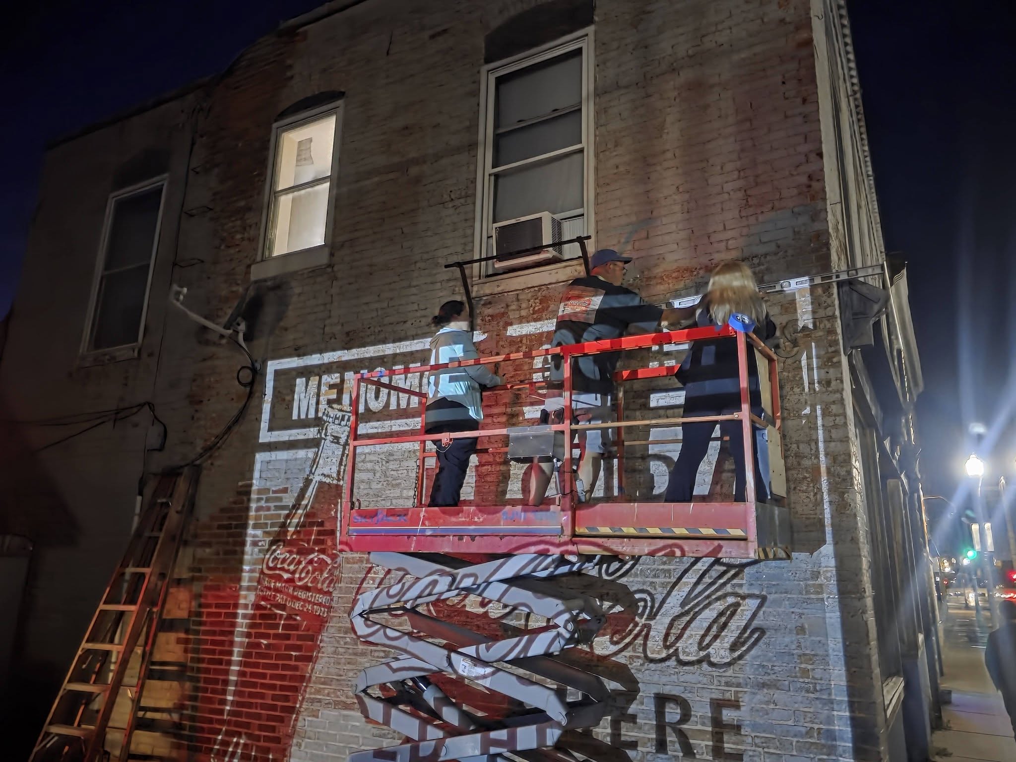 Artists at night in a scissor lift sketching out artwork that is projects onto the wall
