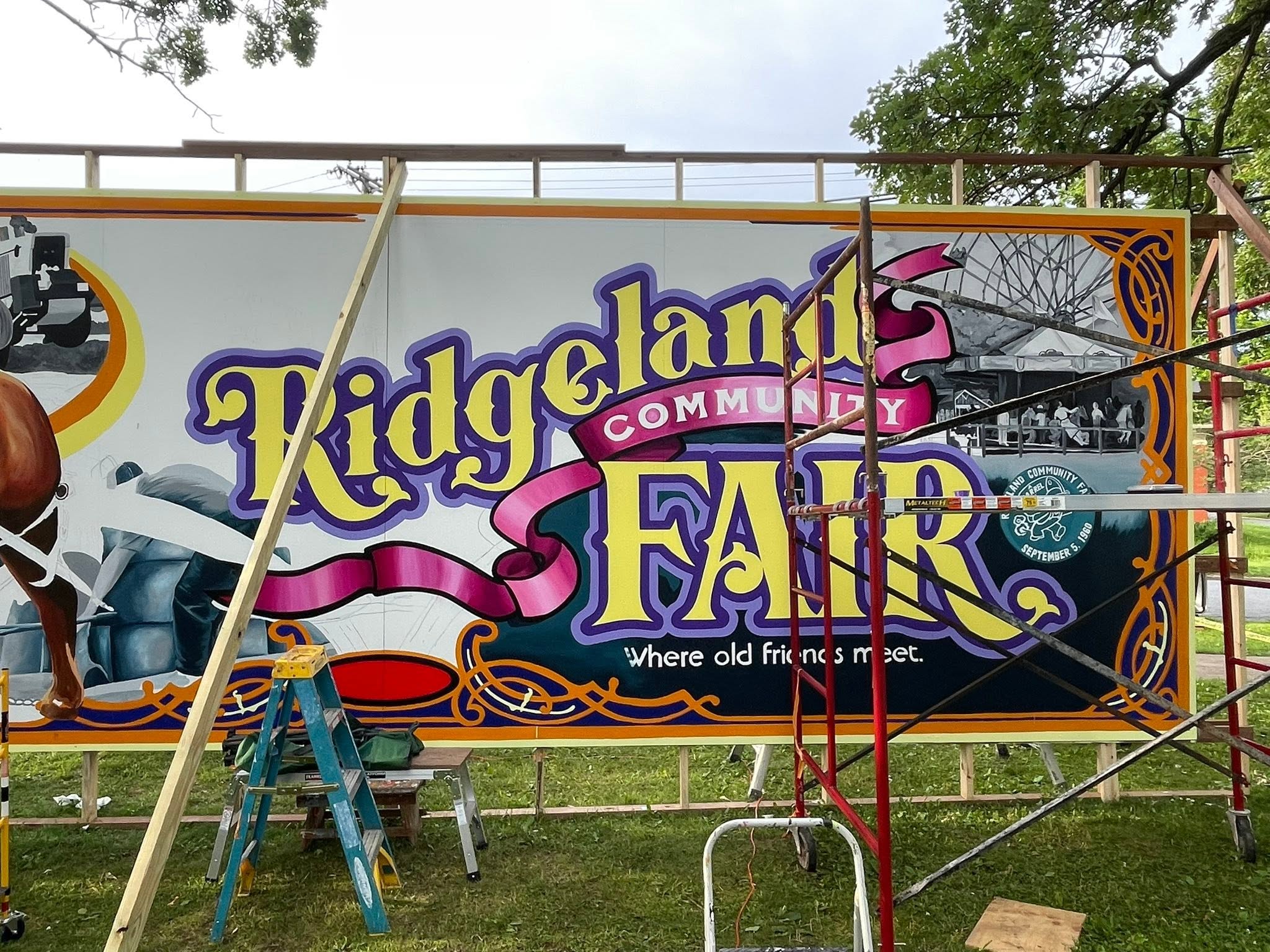 Ridgeland Community Fair mural in the process of being created on wooden frame with ladders and scaffolding