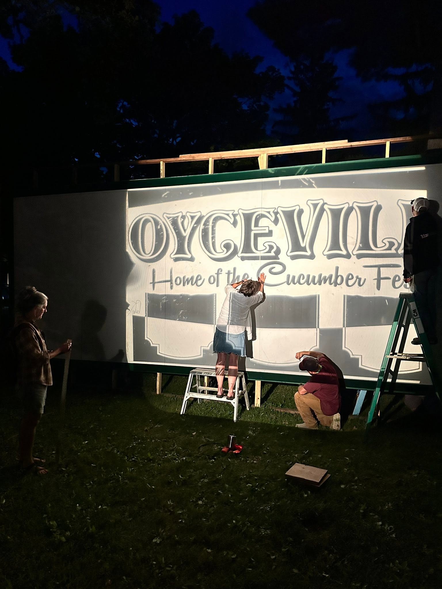 Artists trace artwork for mural at night while image is projected onto the screen
