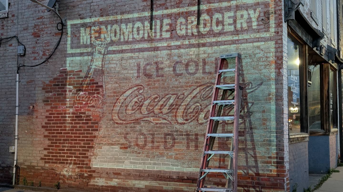 Artwork for mural is projected onto the wall for the Menomonie Grocery Ice Cold Coca Cola Sold Here sign
