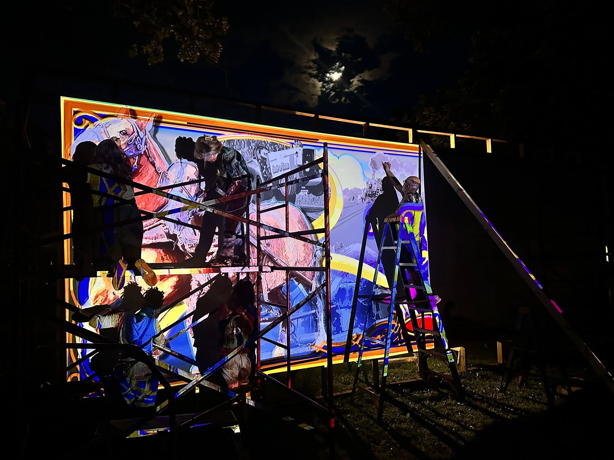 Artists painting and sketching at night while artwork is projected onto area