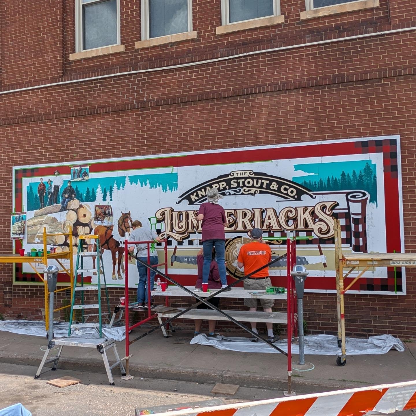 Multiple artists painting a mural with ladders and scaffolding
