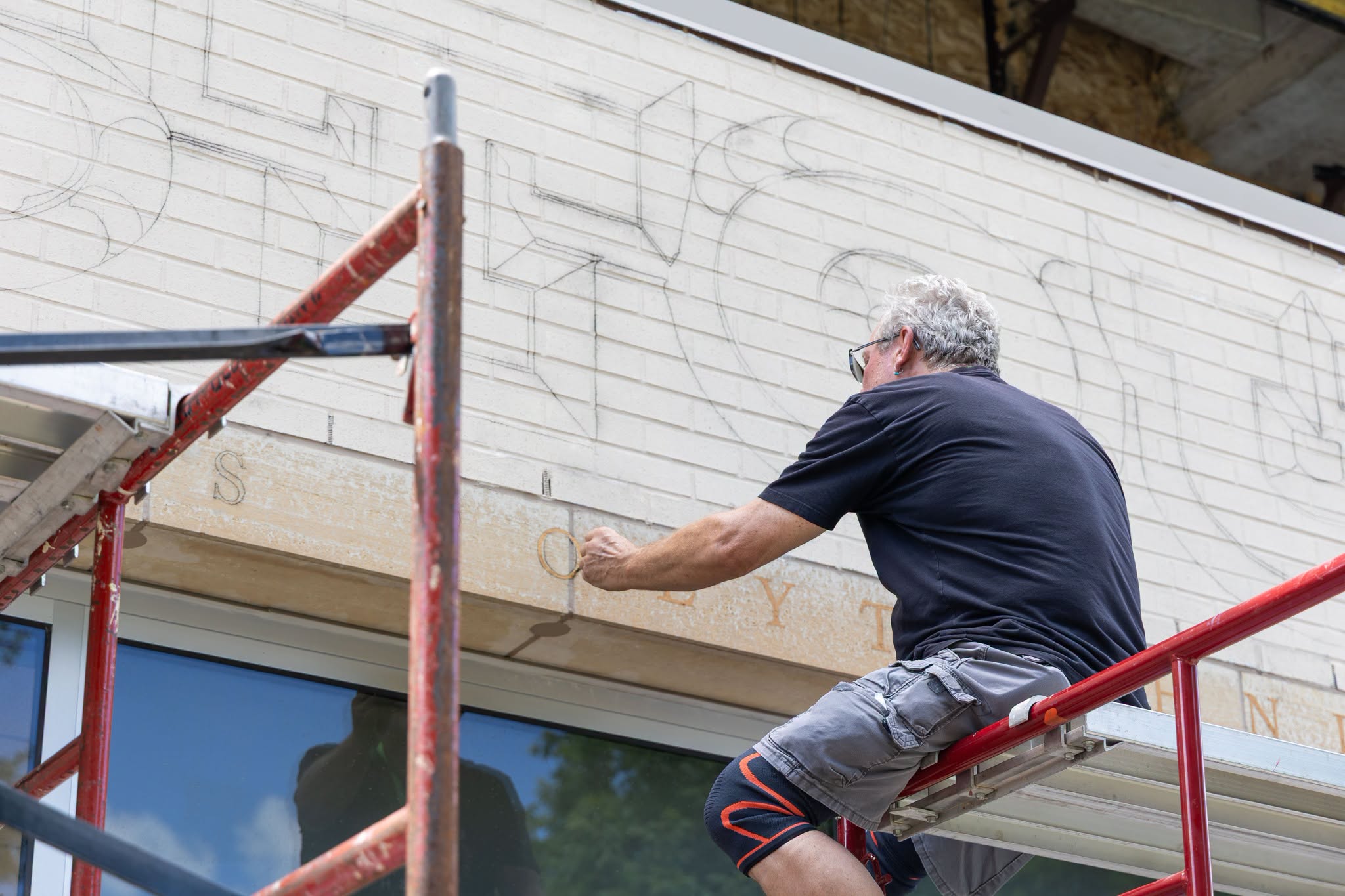 Artist sitting up high painting letters for a mural