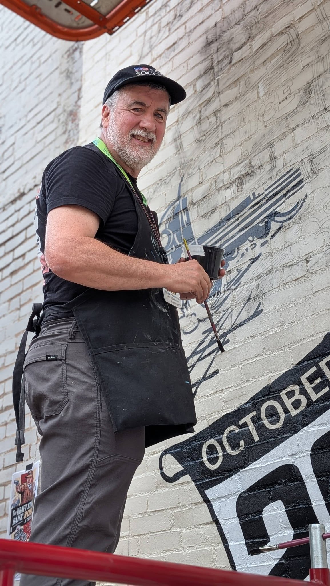 Artist in black and gray standing and painting a mural