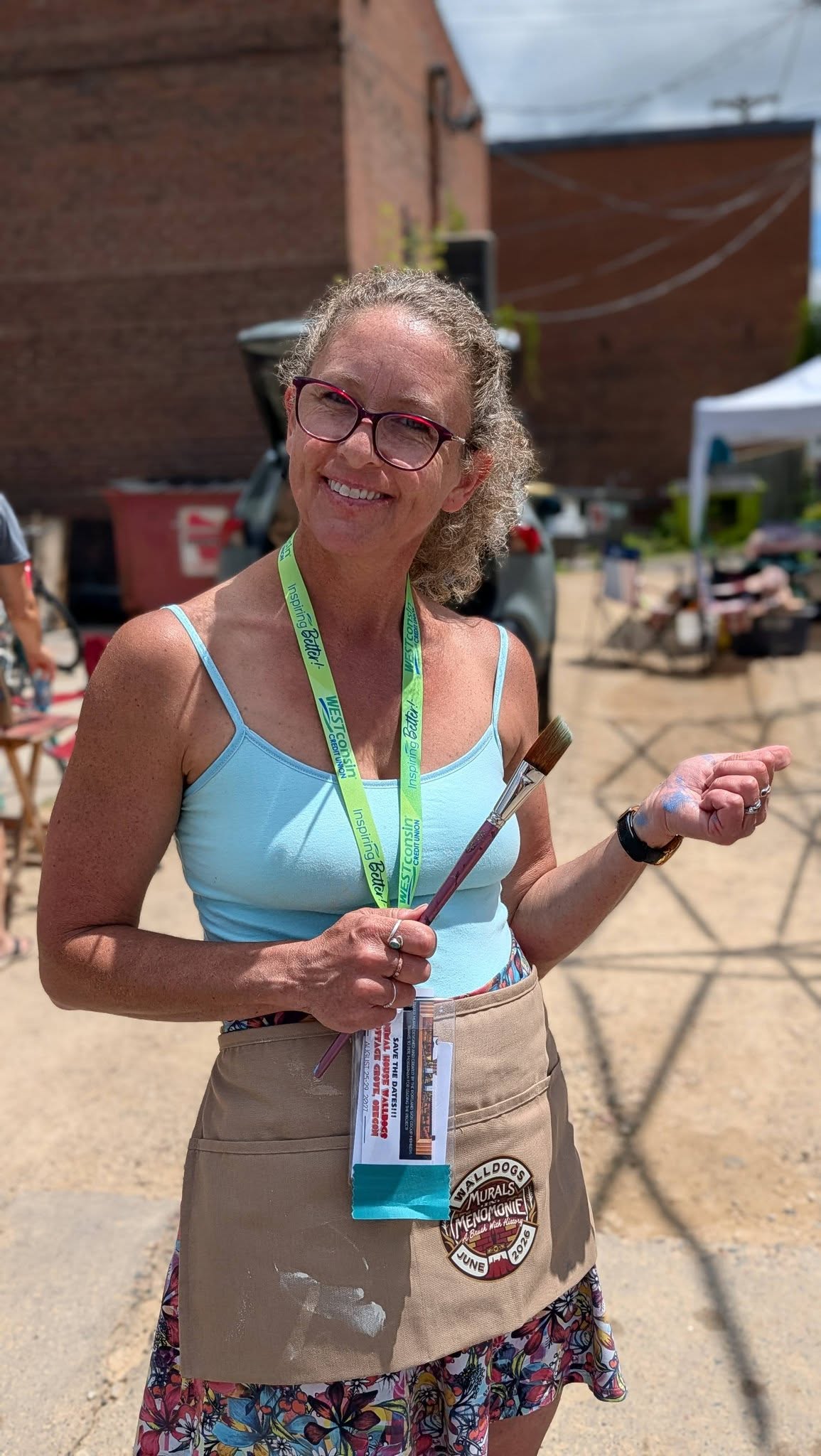 Woman wearing an apron and lanyard holding a paint brush