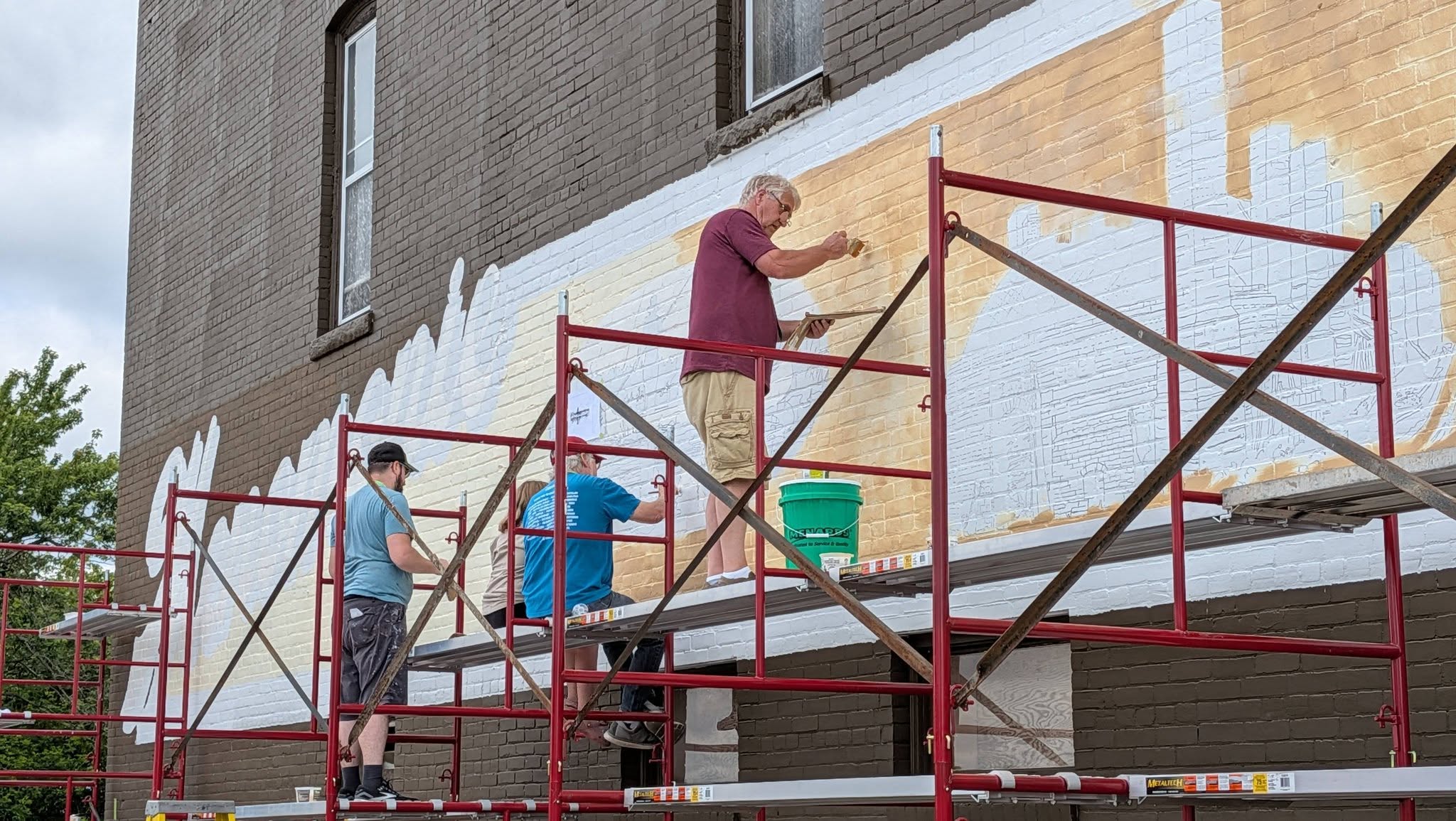 Multiple Artists sitting and standing on scaffolding while painting a mural