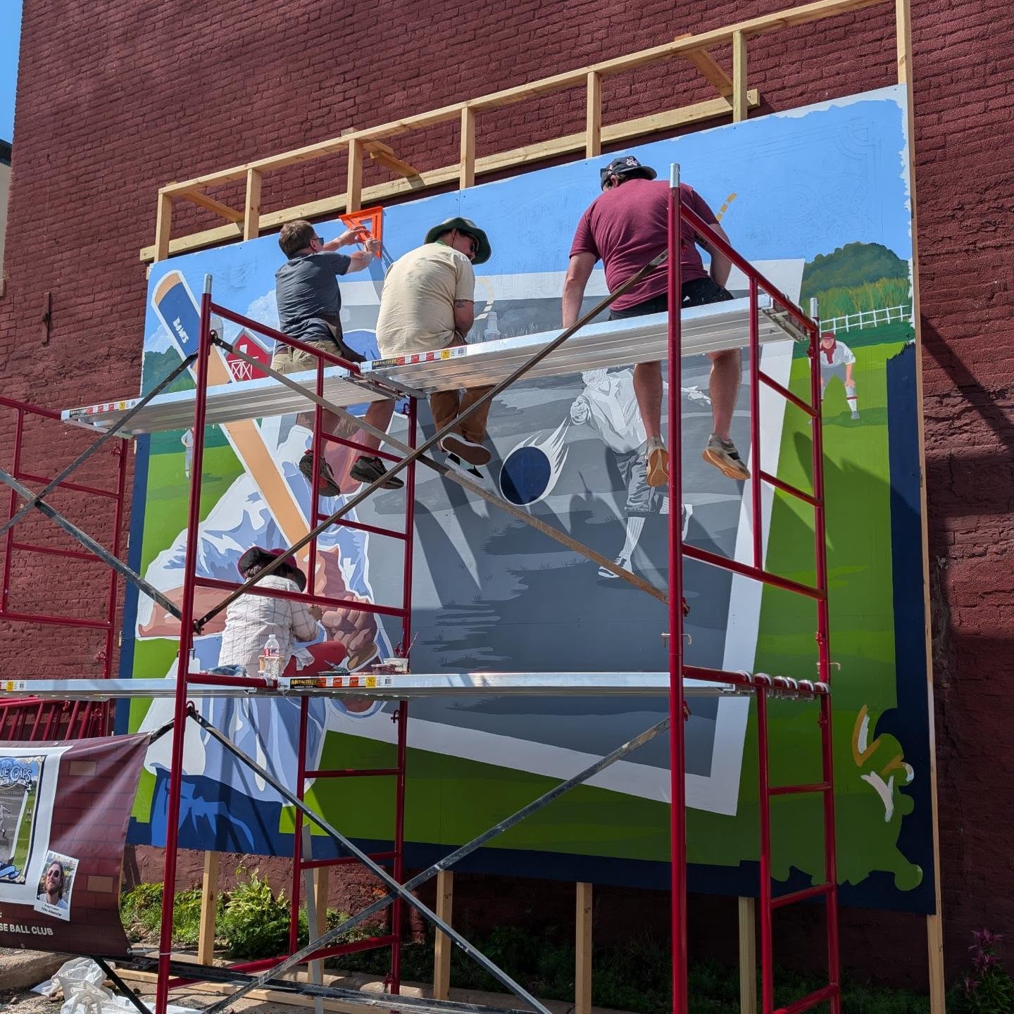 Multiple Artists sitting on scaffolding while painting a mural