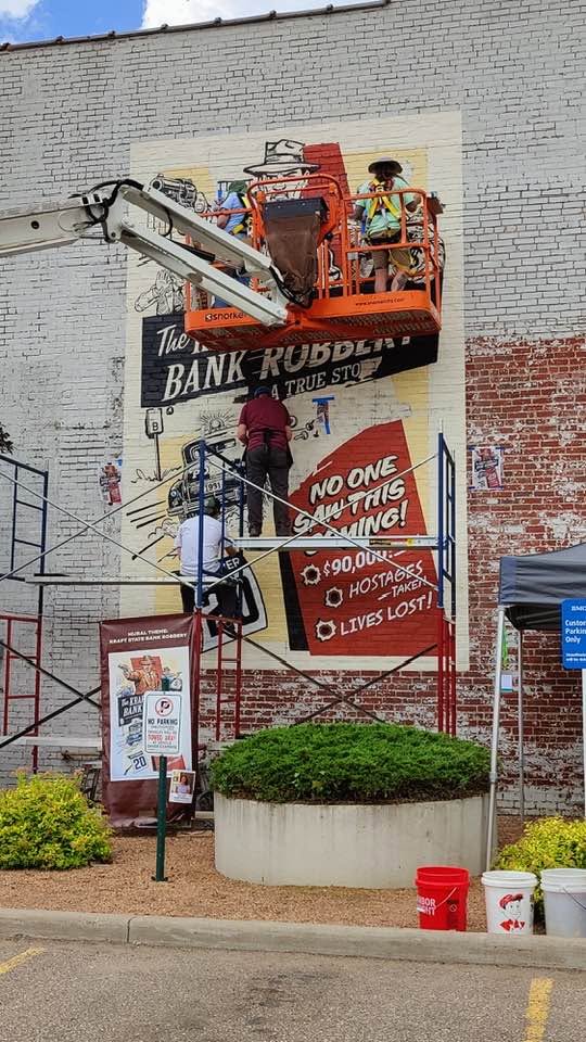 Artists at various levels on scaffolding and in a lift painting a mural