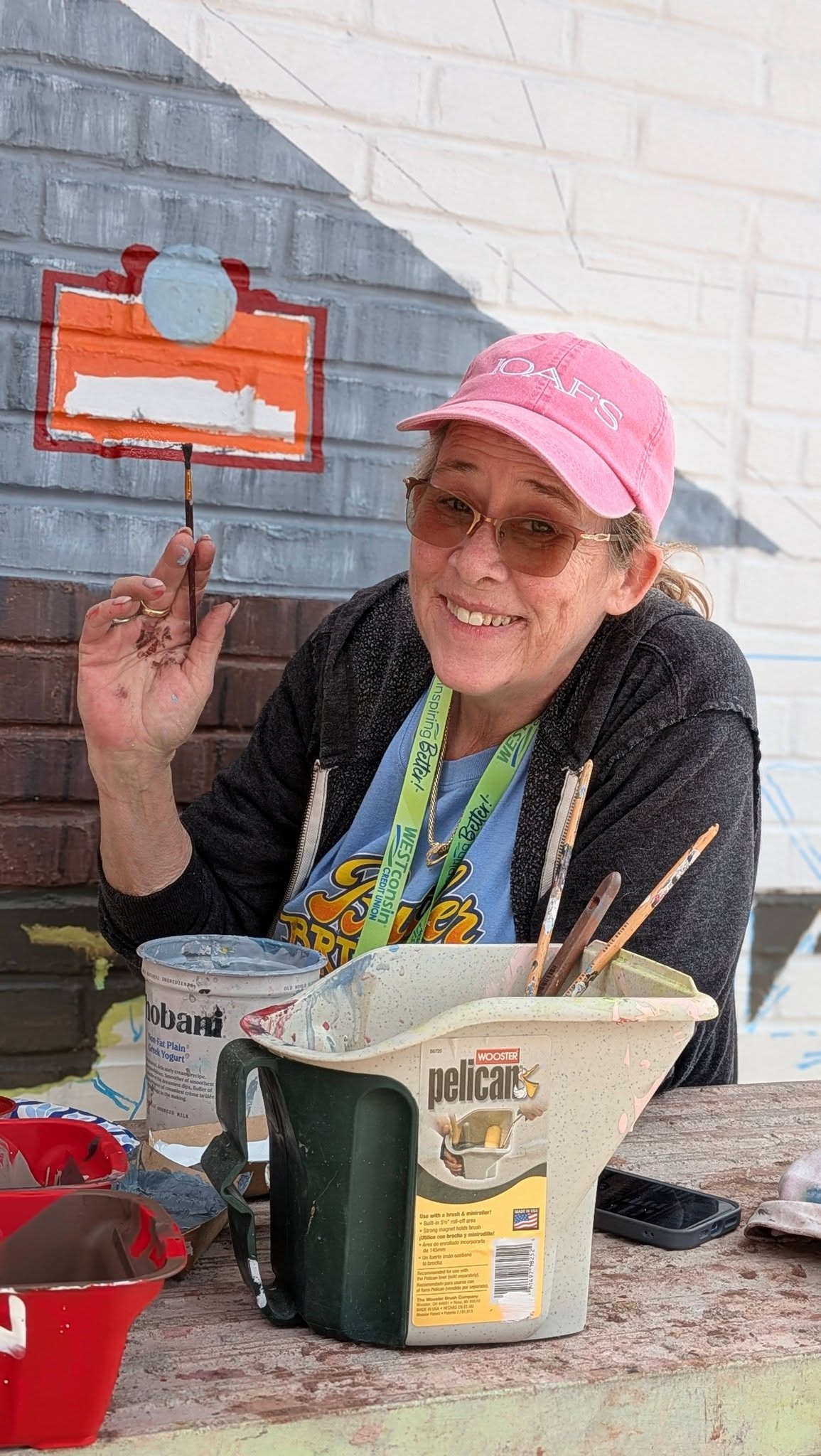 Woman in pink hat waving with a paintbrush