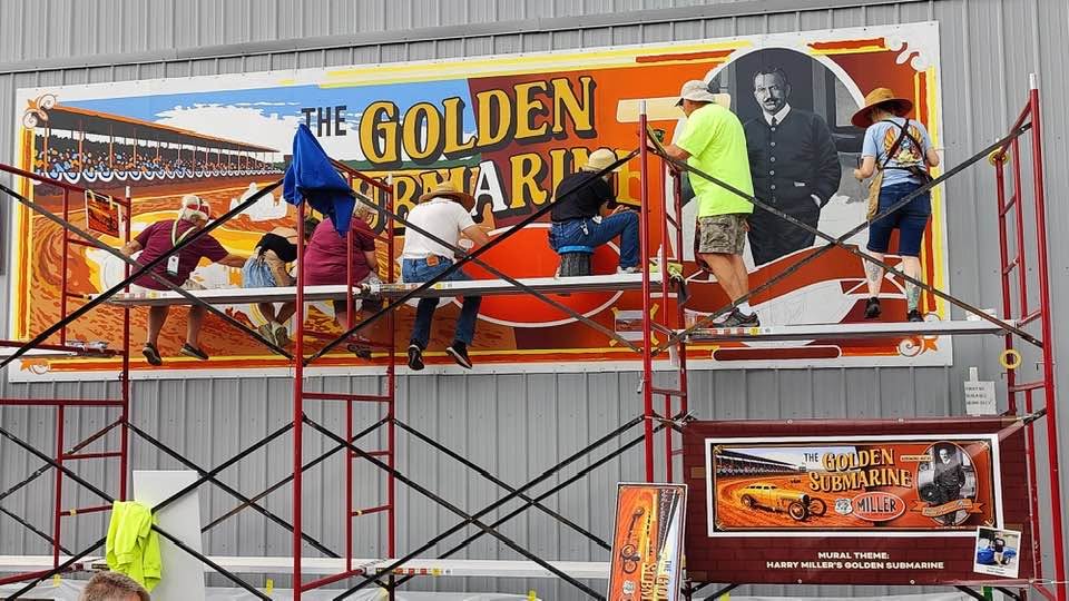 Multiple Artists sitting and standing on scaffolding while painting a mural