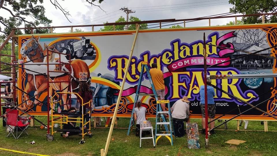 Artists at different spots of mural paint while on scaffolding and ladders