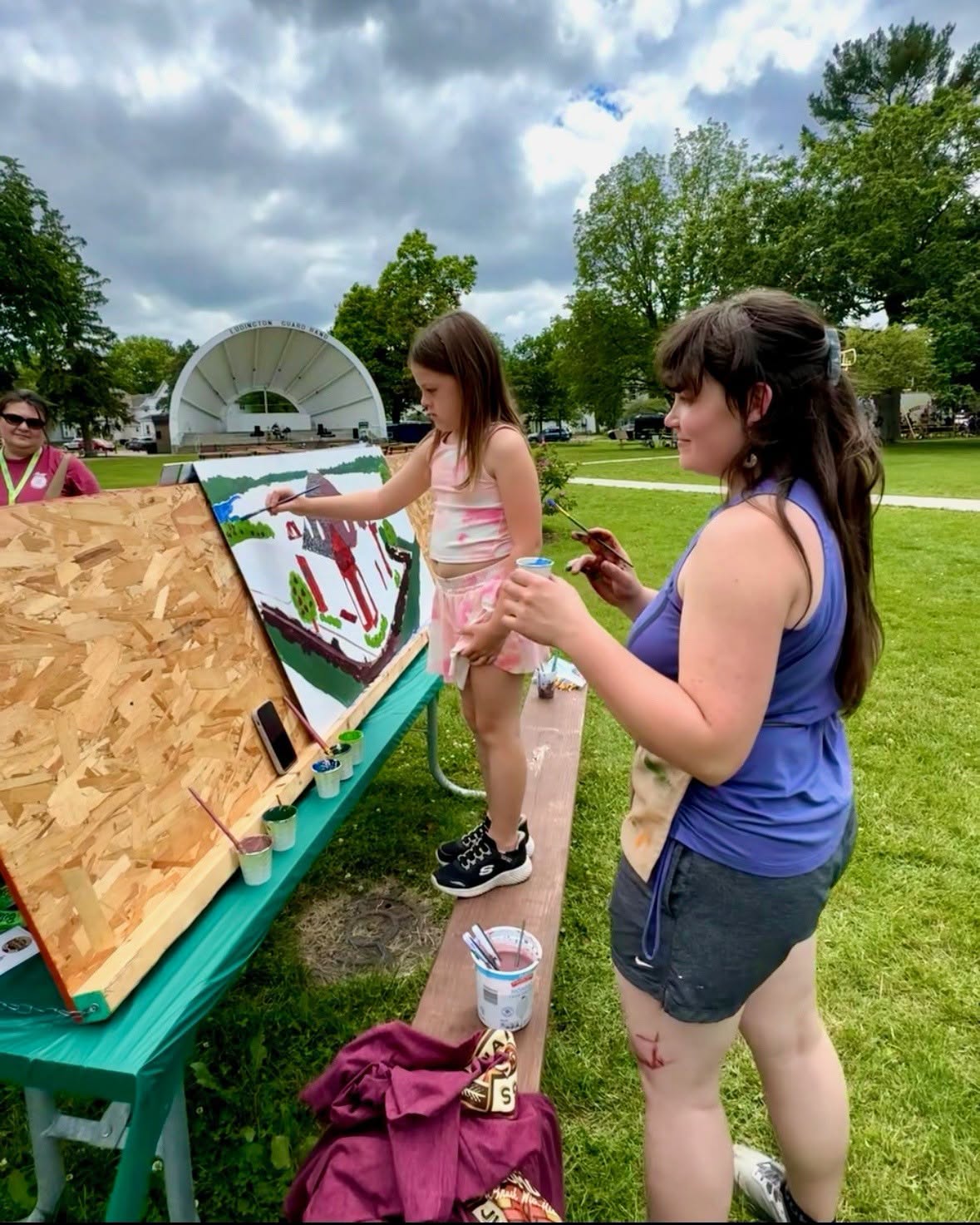A woman and a little girl paint a picture on top of a picnic table
