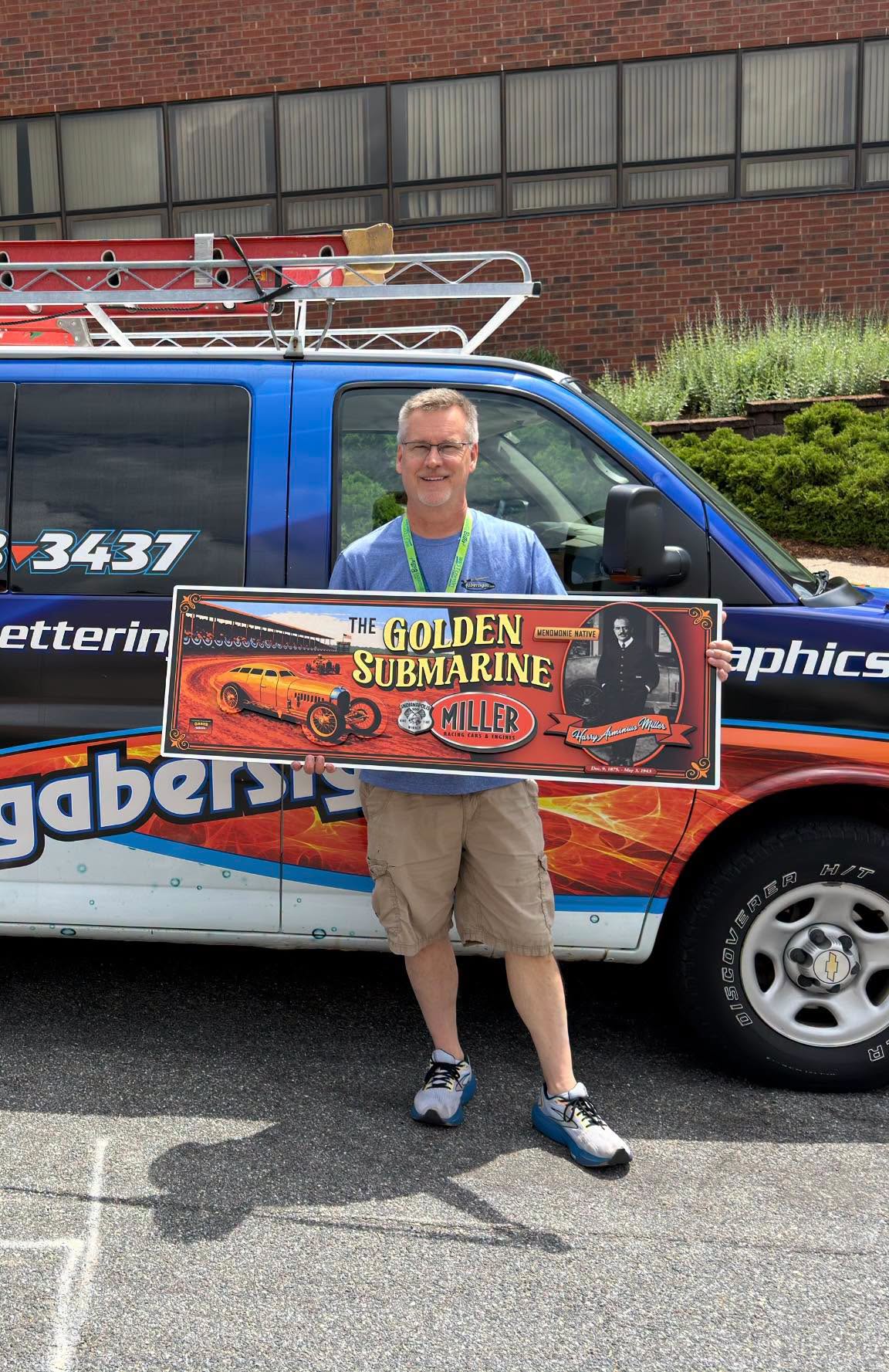 Man standing in front of a vehicle holding a painted replica of the Golden Submarine mural