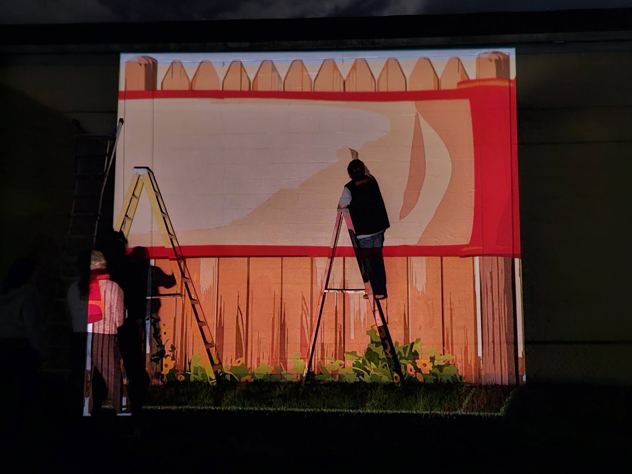Person on a ladder painting in the dark with image projected on to the wall