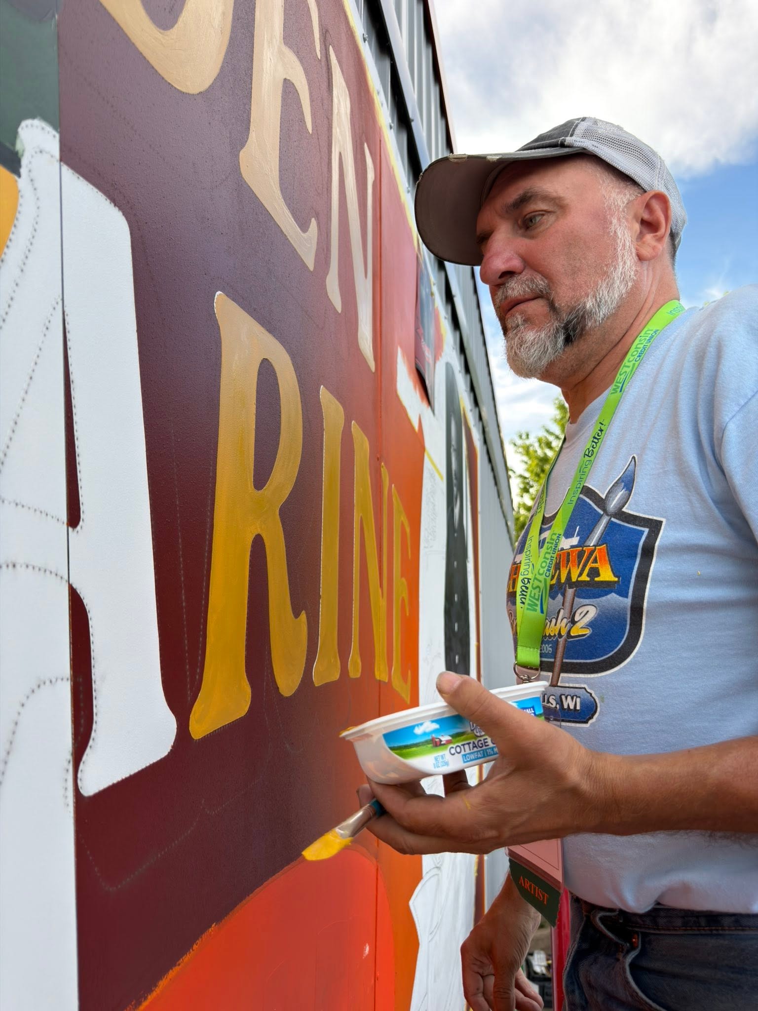 Man in front of a mural holding dish of paint