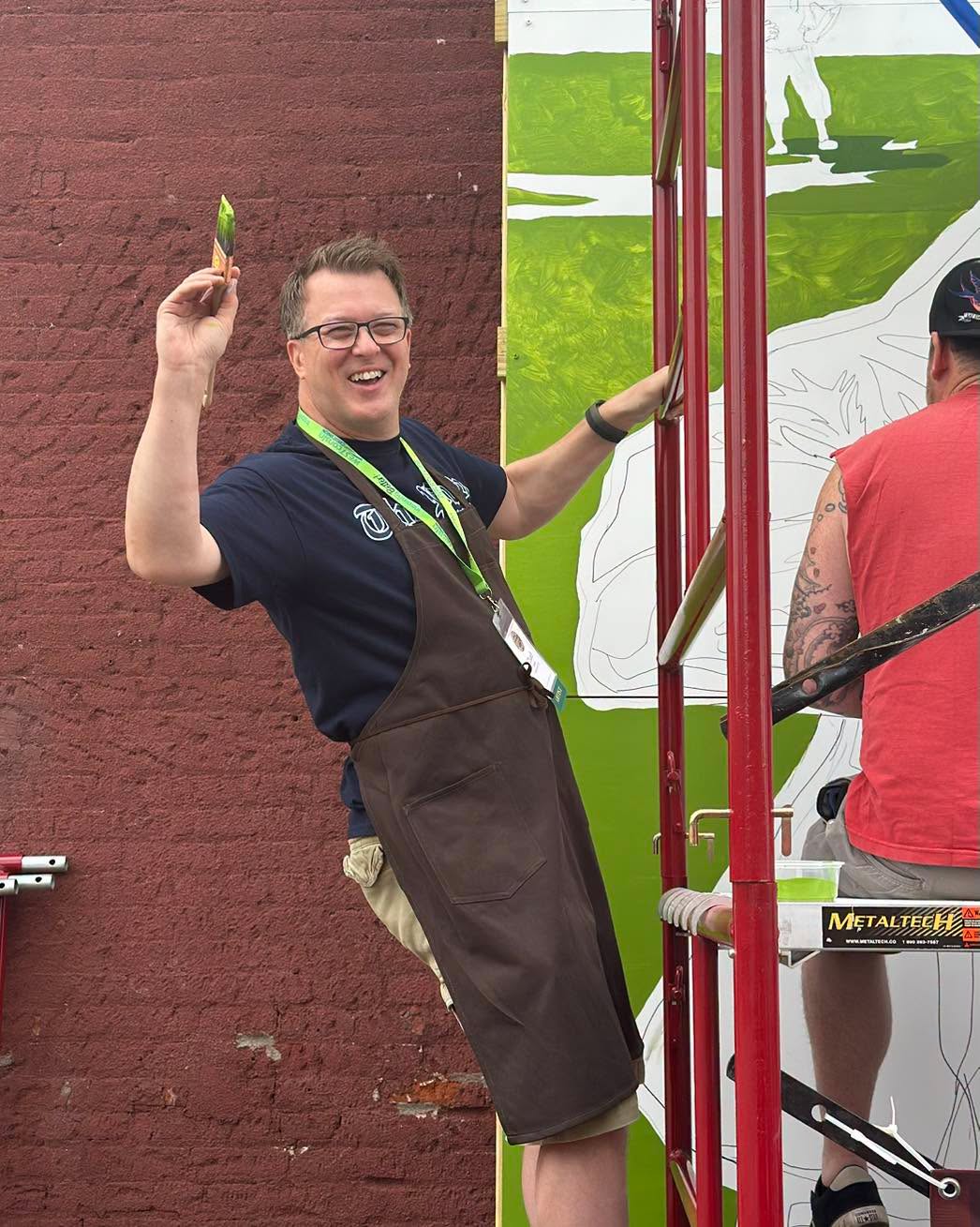 Artist hanging from scaffolding waving a paint brush