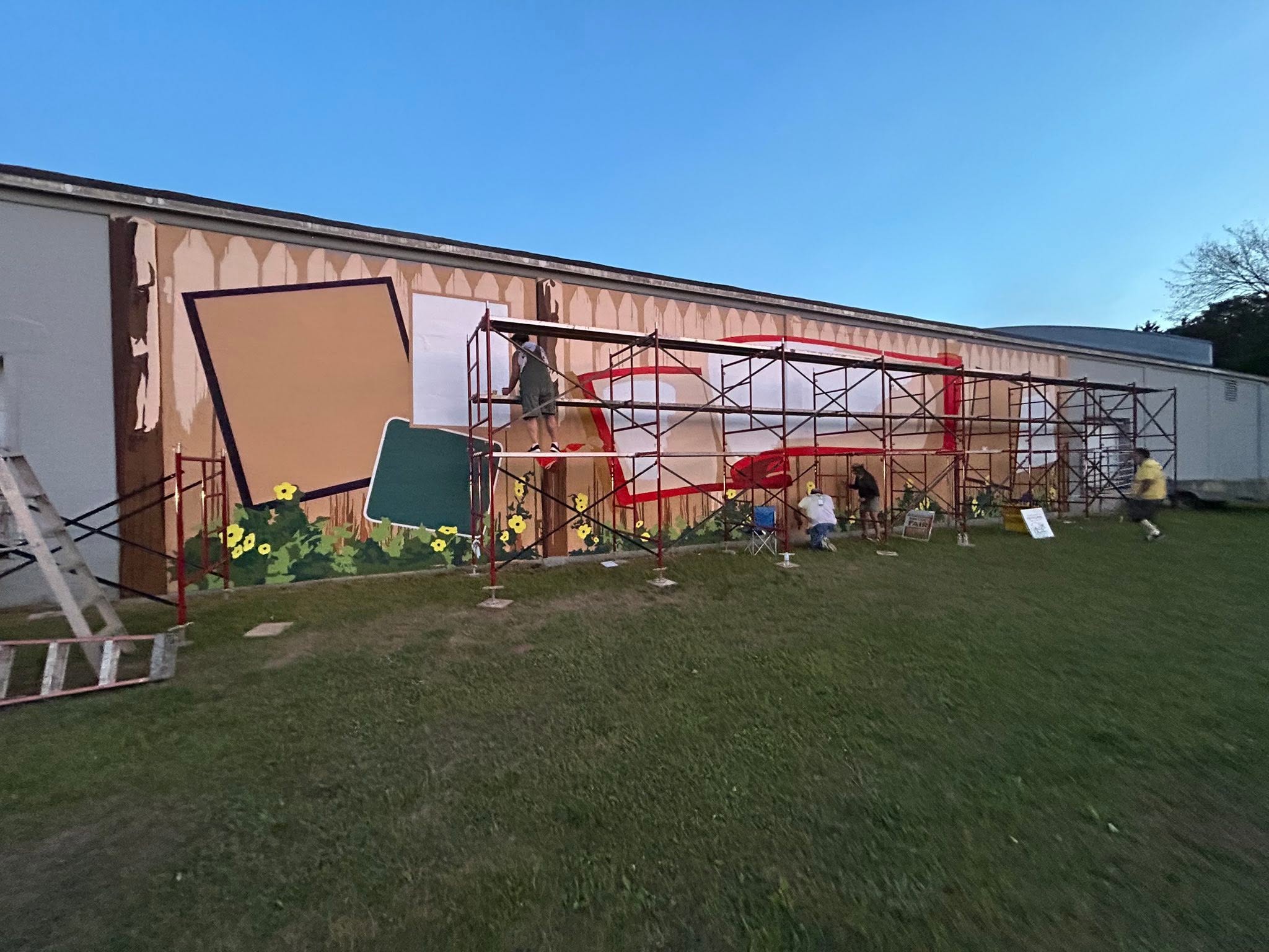 Scaffolding in front a mural getting painted in a grassy area