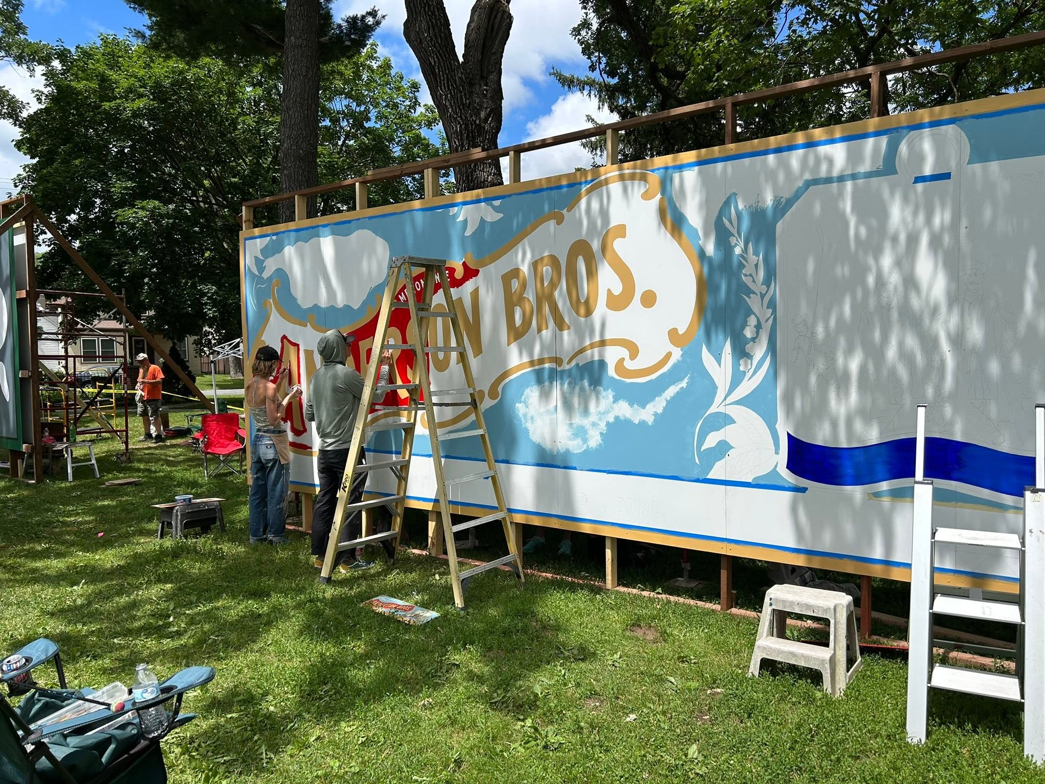 People and ladders in front of a mural getting painted