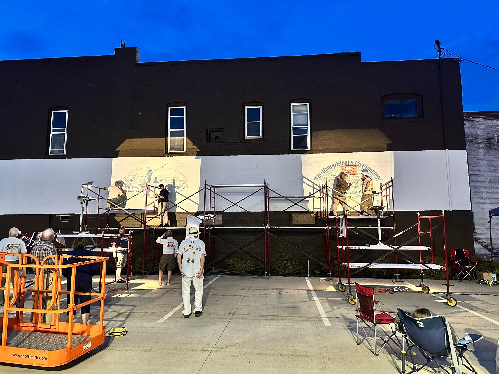 People gathered to watch artists on scaffolding draw on walls from lighted projectors