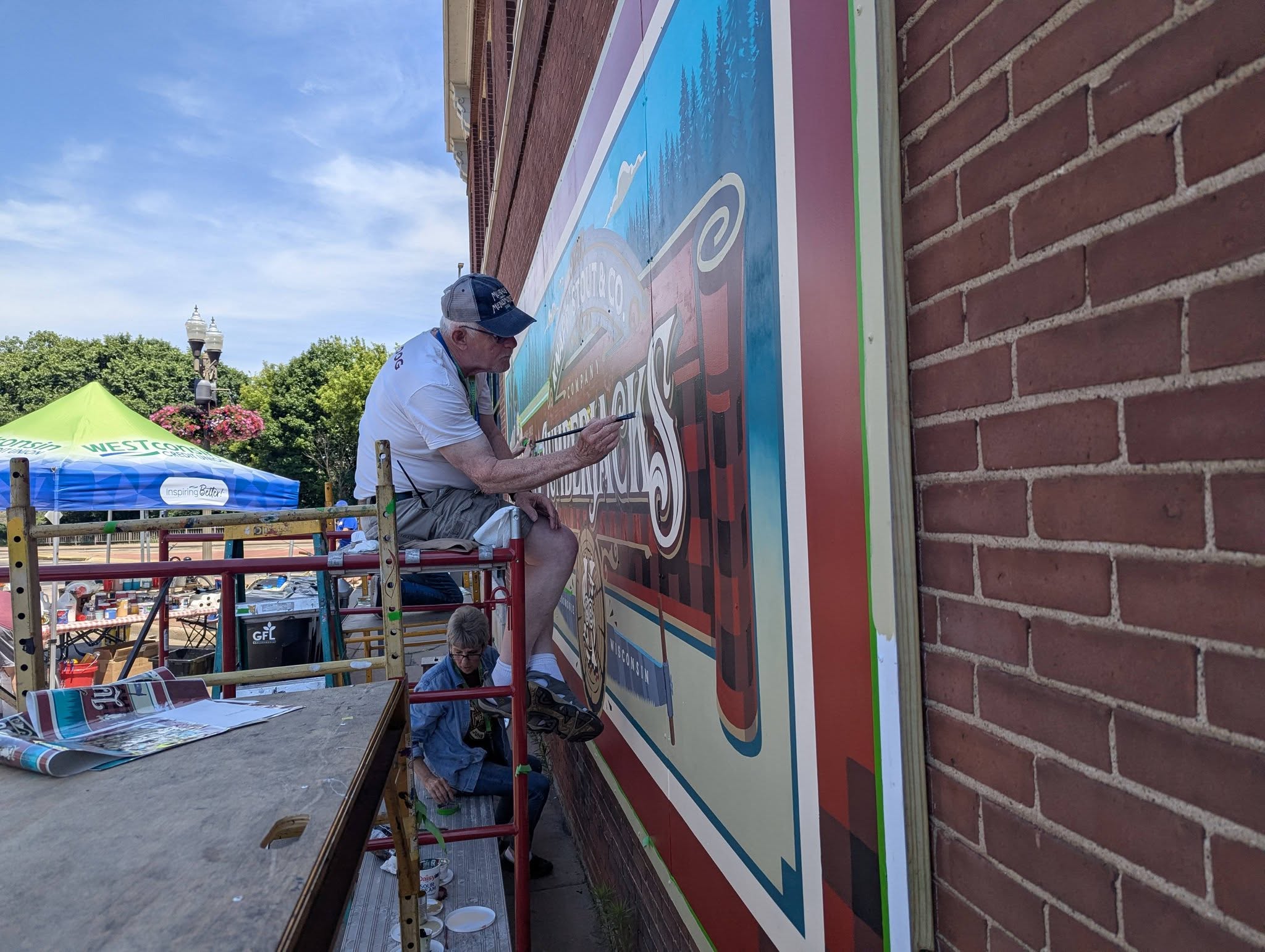 Man sitting on top of scaffolding painting a mural