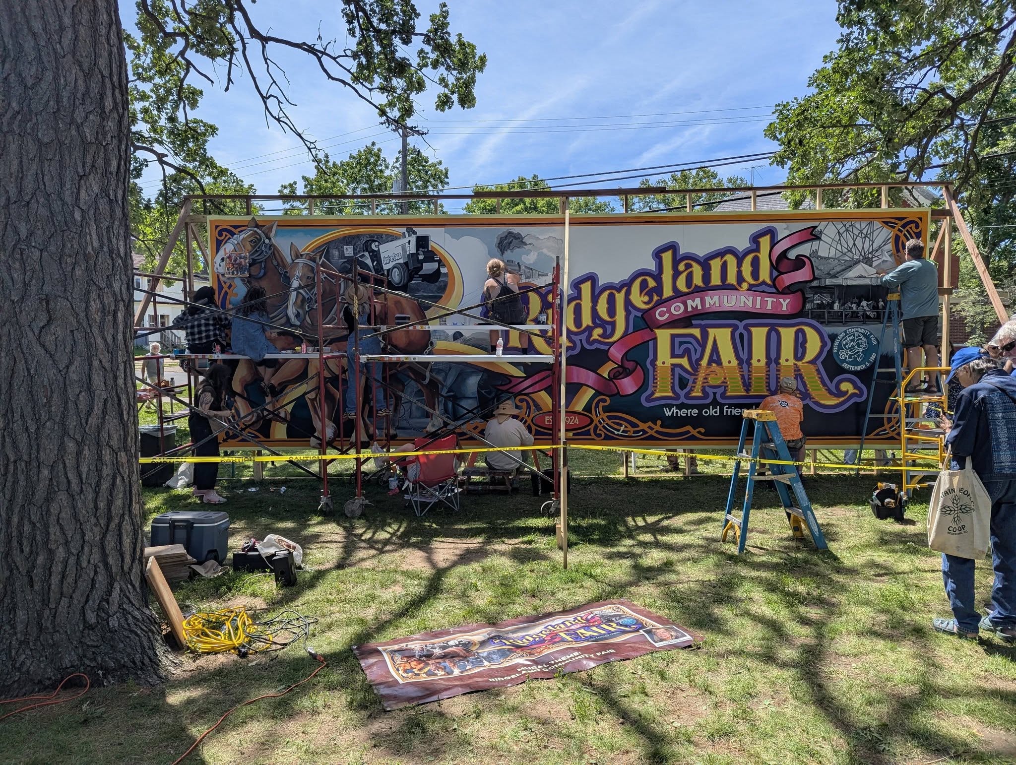 Scaffolding and painters in front of the Ridgeland Community Fair mural