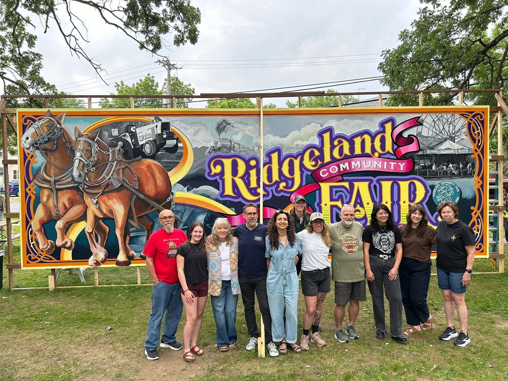 Group of people posing in front of the Ridgeland Community Fair mural with horses pictured