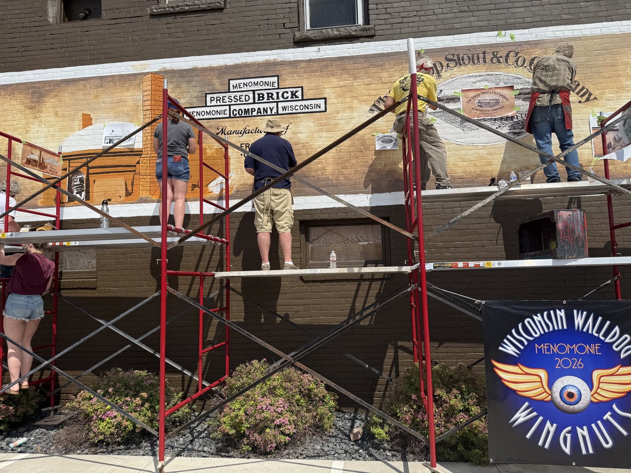 Artists standing on scaffolding while painting a mural