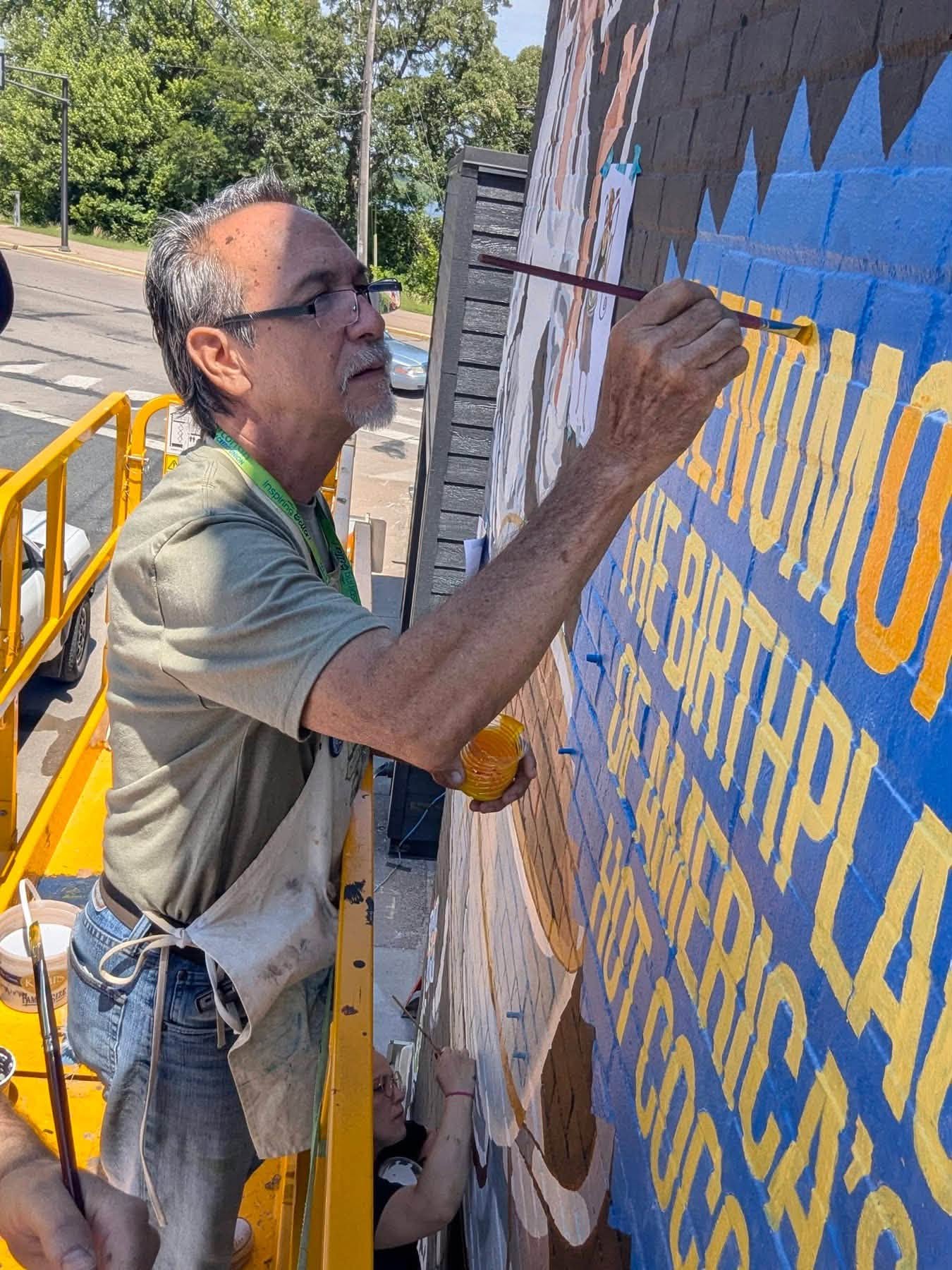 Man painting yellow letters on a mural