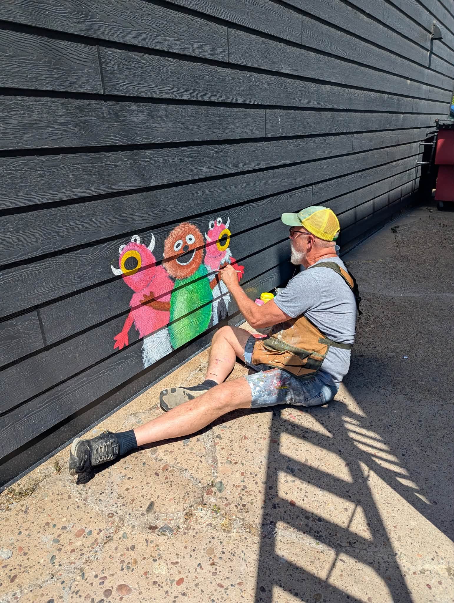 man sitting on the ground painting small monsters on a wall