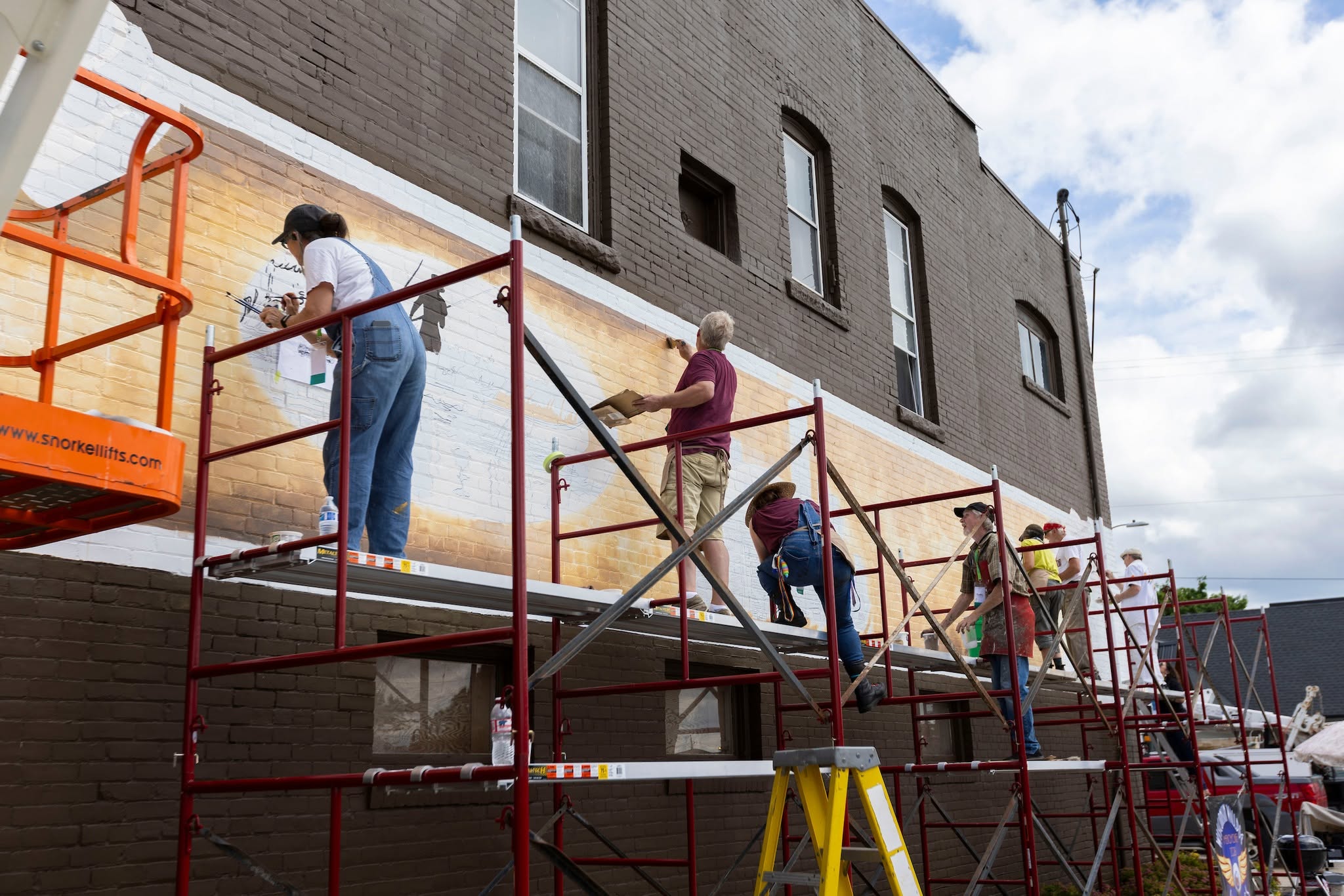 group of artists spread out across scaffolding painting a brick wall
