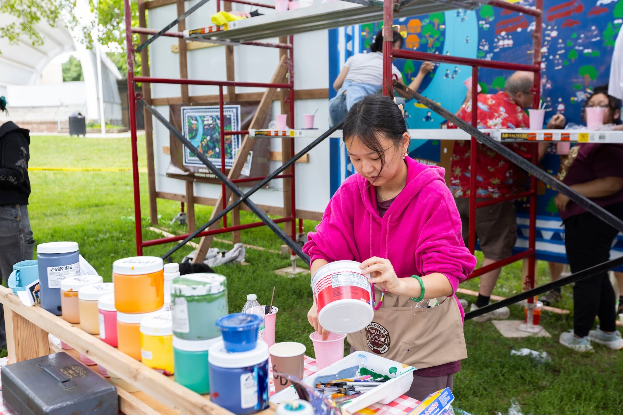 girl pouring paint at a table with canisters of different colors of paint