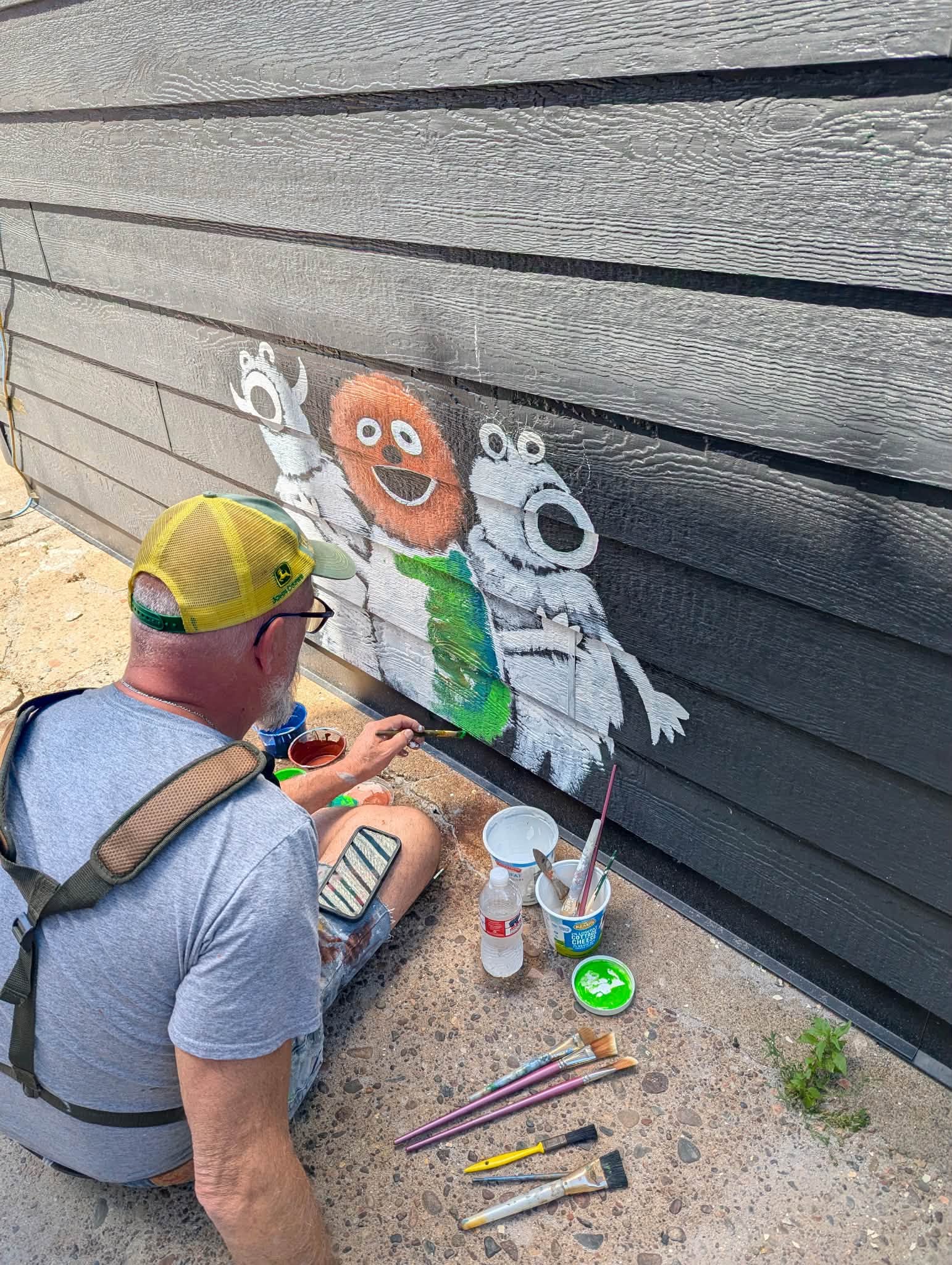 man sitting on the ground painting small monsters on a wall