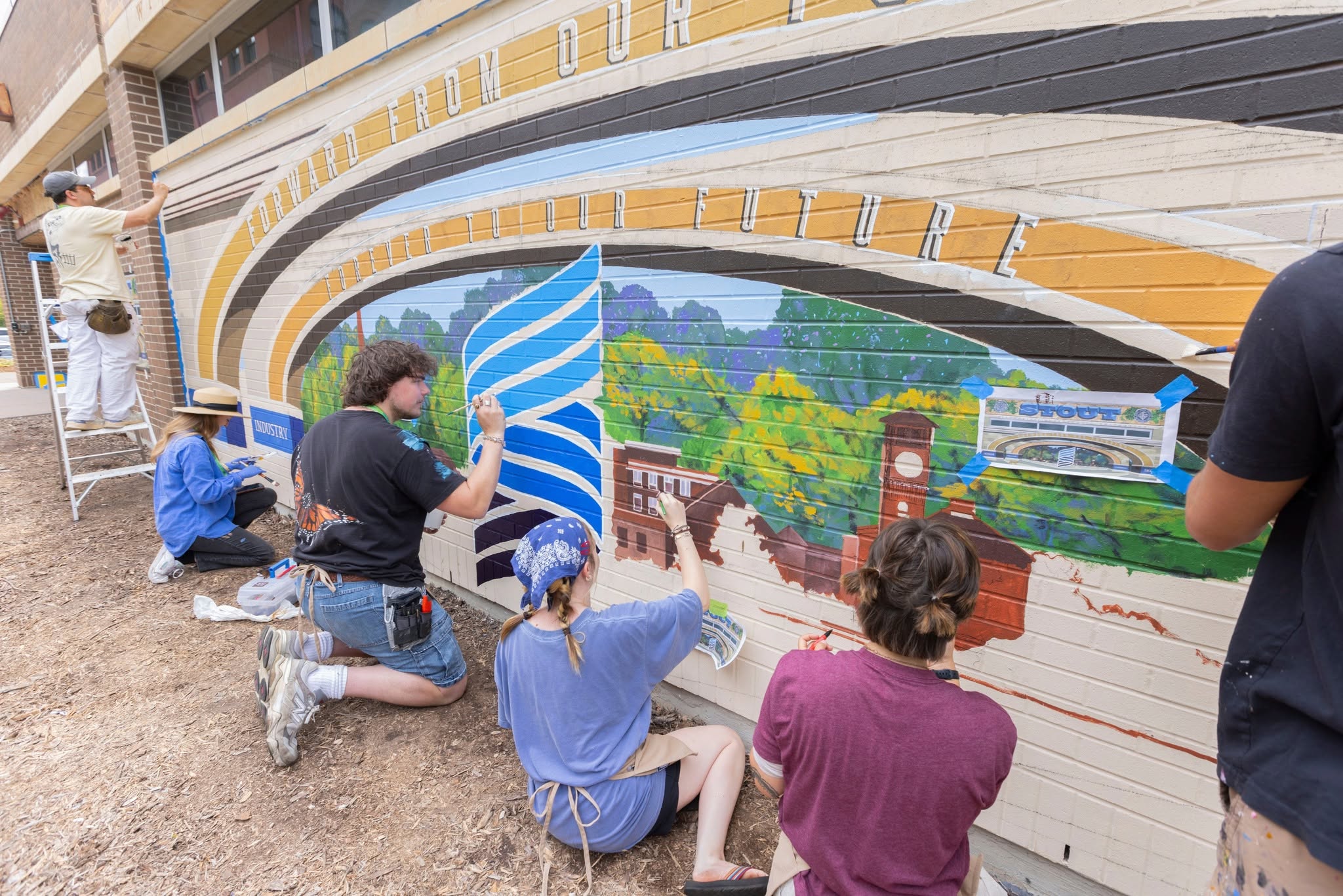 Group of artists spread out painting a mural on a brick wall