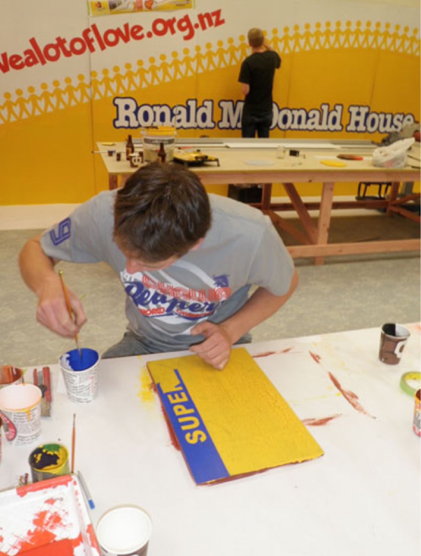 Person dipping brush into blue paint in front of a sign being painted