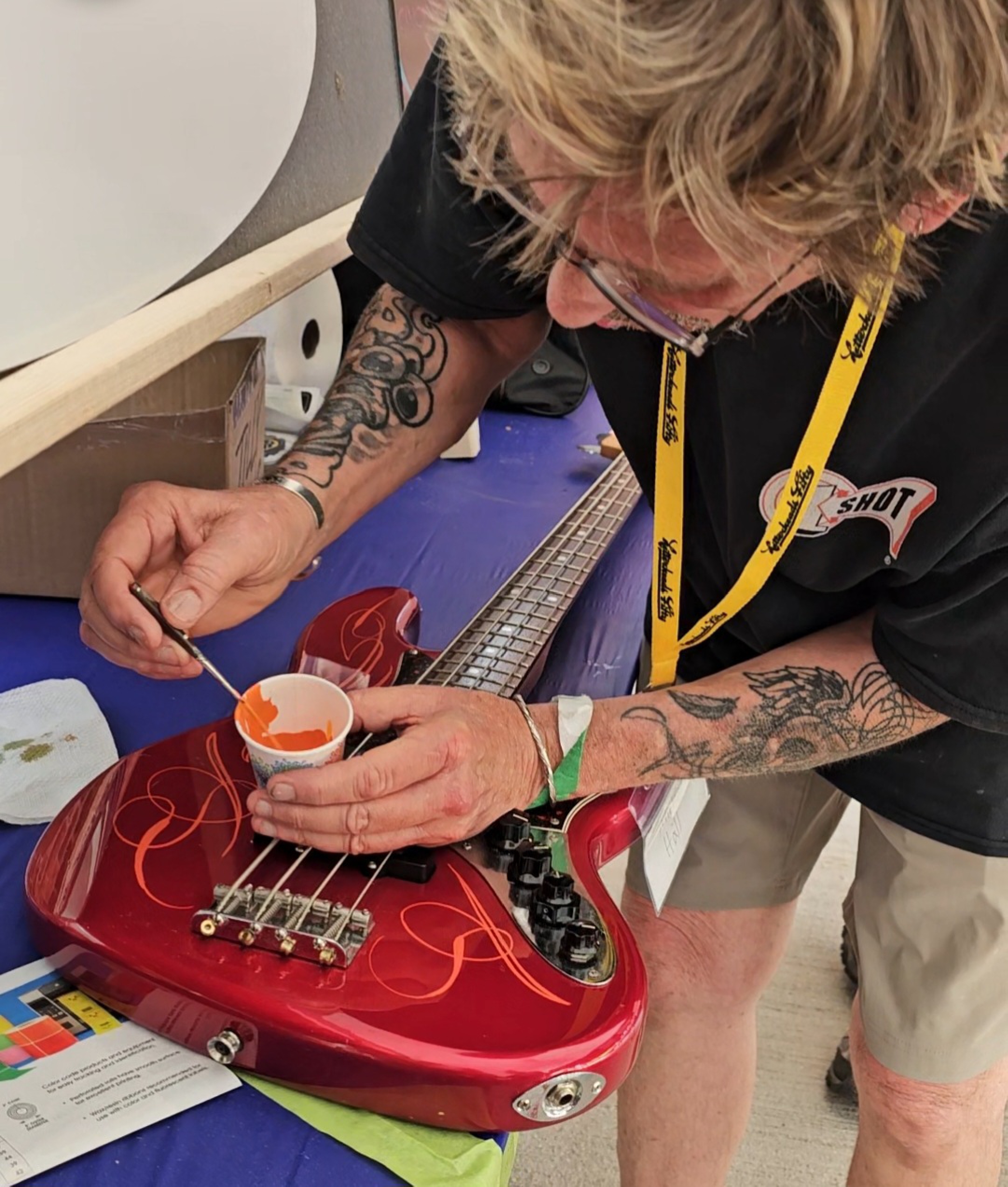 person dipping paintbrush into cup of paint on top of a guitar being painted